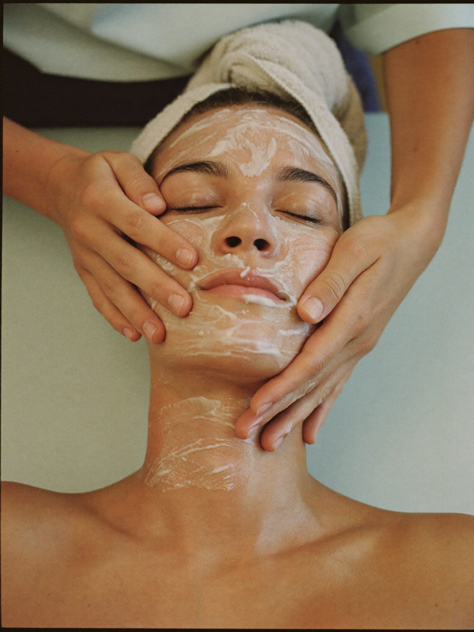 A facial treatment in progress: hands massaging cleanser across a person's cheeks and jawline