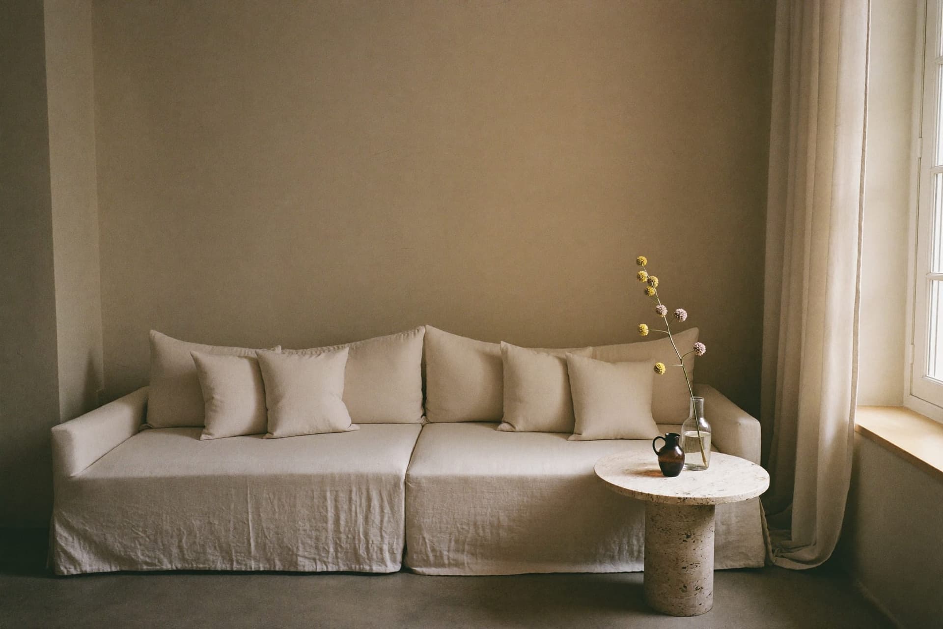 A waiting area in natural light with a low linen sofa and a stone side table